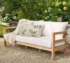 a white couch sitting on top of a gravel covered ground next to trees and bushes