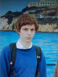 a young man standing in front of a body of water