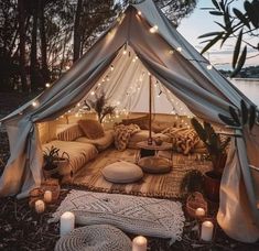 a tent with lights and pillows on the ground next to some candles in front of it