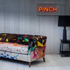 a couch with colorful paint splattered on it in front of a neon sign