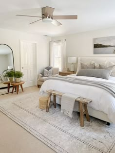 a bedroom with a large bed, mirror and two stools in front of it