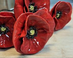 three red ceramic flowers sitting on top of a wooden table next to a potted plant