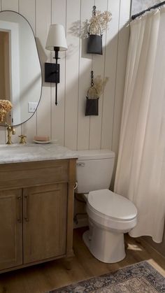 a white toilet sitting next to a sink in a bathroom under a large round mirror