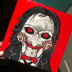 a painting of a creepy clown with red eyes and black hair is being held up