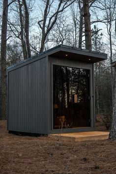 a small shed in the middle of a forest with trees around it and lights on