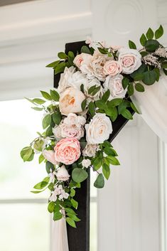 a cross decorated with flowers and greenery in front of a window at a wedding