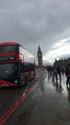 a red double decker bus driving down a wet street