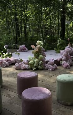 several stools and flower arrangements on a wooden deck in front of some tall trees