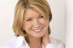 a woman with blonde hair is smiling and wearing a white button up shirt, she has her hand on her chin