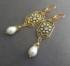 Capturing the romantic elegance of the Renaissance Victorian style, these white pearl teardrop chandelier earrings will make a perfect accessory for any dress occasion. Exotic and sophisticated these classy earrings will bring you a lot of attention and make a perfect addition to your jewelry collection. These gorgeous long dangle earrings feature delicate antique gold with intricate Art Deco style design pendants paved with tiny creamy white pearls and a crystal rhinestone in the center sending sparkles with the slightest movement. A matching large glass pearl teardrop dressed in antique gold filigree bead caps is suspended from the pendant.  The length from the top of vintage-style gold tone secure lever back ear wires is 3" (7.5 cm). The ear wires are lead and nickel-free suitable for t Vintage Dangle Earrings, Teardrop Chandelier, Classy Earrings, Intricate Art, Bling Earrings, Gold Bridal Earrings, Earrings Antique, Long Dangle Earrings, Dress Occasion