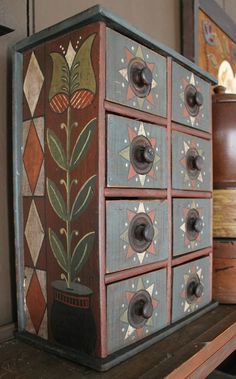 an old wooden box with flowers painted on it's sides sitting on a shelf