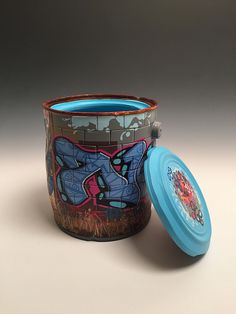 a cup with graffiti on it next to a blue lid