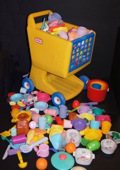 a toy shopping cart filled with toys on top of a black table next to cups and saucers