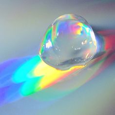 a drop of water that is sitting on top of a rainbow colored table cloth with the light coming through it