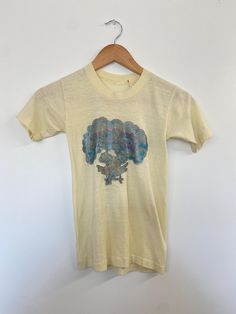 * Era: 70s * Label: None * Size: XXS * Material: Cotton * Condition: good vintage condition! INFO~ *Butter yellow baby tee of your dreams! *Fun, playful, girlhood vibes from this graphic glitter tee! *Faded but still fully legible, this cosmic cutie tee would be a great closet staple! CONDITION~ Flaws noted: good condition with slight discoloration on the back left sleeve + a small white spot on the back as well. Glitter is faded but still brings the sparkle and shine.  SIZING~ Pit to pit: 12" S Vintage Yellow Tops With Screen Print, Vintage Yellow Top With Screen Print, Yellow Vintage Crew Neck Top, Retro Yellow Tops With Vintage Print, Vintage Yellow Short Sleeve T-shirt, Glitter Tee, Graphic Baby Tee, Yellow Baby, Baby Graphic Tees