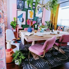 a dining room table with pink chairs and pictures on the wall in the back ground