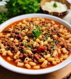 a white bowl filled with pasta and ground beef soup on top of a wooden cutting board