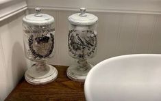 two glass jars sitting next to each other on a wooden table in front of a white sink