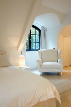 a white bed sitting under a window next to a chair in a room with an arched ceiling