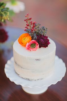 a white cake topped with flowers on top of a wooden table next to red and orange flowers