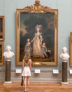 a woman standing in front of a painting on display with busturines behind her