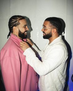 two men standing next to each other in front of a white wall and one is tying the jacket