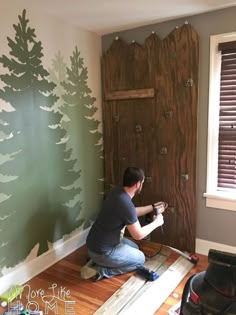 a man painting a wall with pine trees on it