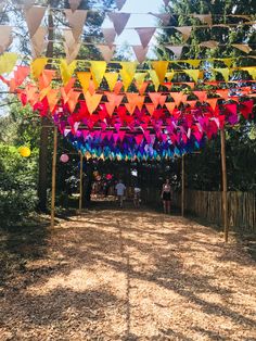 an outdoor area with many colorful flags hanging from the ceiling and people walking under it