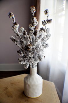 a white vase filled with flowers on top of a wooden table next to a window