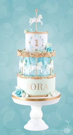 a three tiered cake decorated with blue and white frosting, gold trimmings and a horse on top