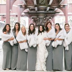 a group of women standing next to each other in long grey dresses and fur stoles