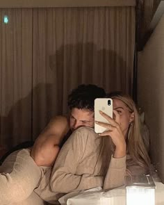 a man and woman laying in bed taking a selfie with their cell phones at night