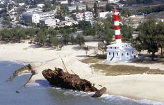 an aerial view of a lighthouse in the water near a sandy beach with houses and trees