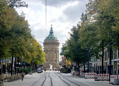 a clock tower in the middle of an empty street with trees lining both sides and people walking on either side