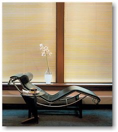 an empty chaise lounge chair in front of a window with blinds on the windowsill