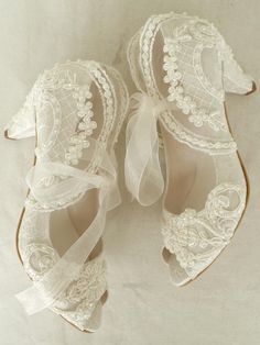 two pairs of white lace shoes with bows on the toes and one shoe has a bow at the top