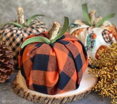 three plaid fabric pumpkins sitting on top of a wooden stump next to pine cones