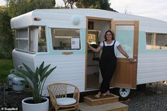 a woman standing in the doorway of an old camper with her hand on the door