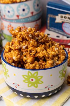 a bowl full of caramel popcorn sitting on top of a table next to two boxes