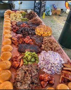 a table topped with lots of meat and hamburgers next to other food on buns