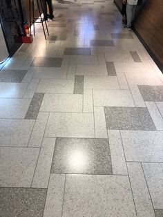 people are walking down an empty hallway with tiled floors and floor tiles on both sides