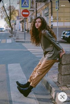 a woman leaning against a wall on the side of a street with her legs crossed