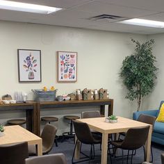 a room with several tables and chairs in front of a blue couch, potted plant on the far wall