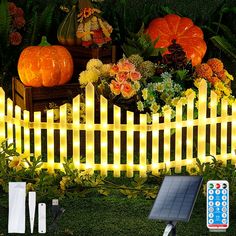 a white picket fence with pumpkins and flowers on the grass next to solar lights