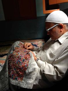 an old man sitting on the floor working on something with scissors and thread in his hand