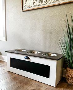 a dog bowl on top of a white cabinet next to a potted plant