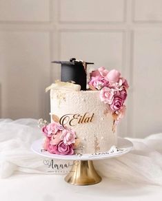 a wedding cake decorated with pink flowers on a white tablecloth and gold plated stand