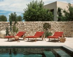 red lounge chairs sitting next to a pool in front of a stone wall and cactus