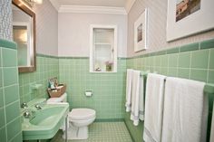 a bathroom with green tile and white towels on the rack above the toilet, along with two framed pictures