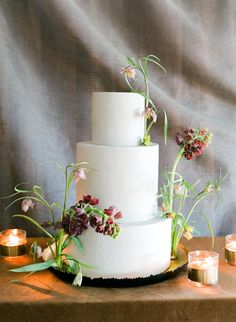 a three tiered white cake with flowers and candles on the table next to it